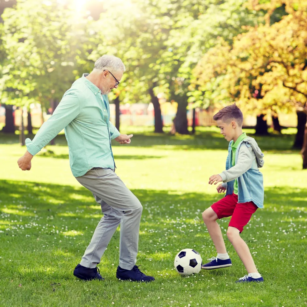 Happy grandfather and grandson playing football at summer park